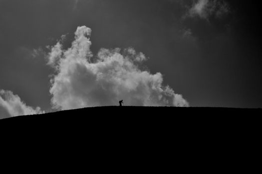 Silhouette of a hiker on a hill under dramatic clouds, captured in black and white.