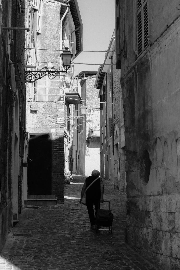 Old Man Walking In Narrow Paved Street