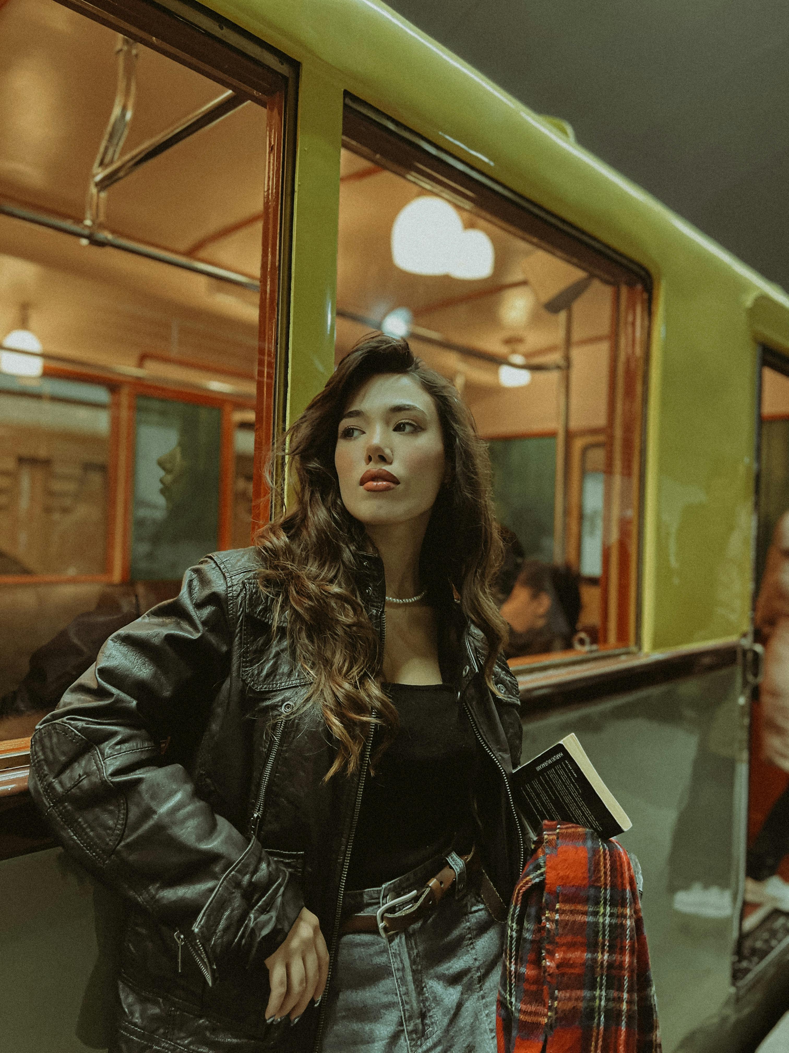 Portrait of a young woman in a leather jacket leaning on a train in Baku station.