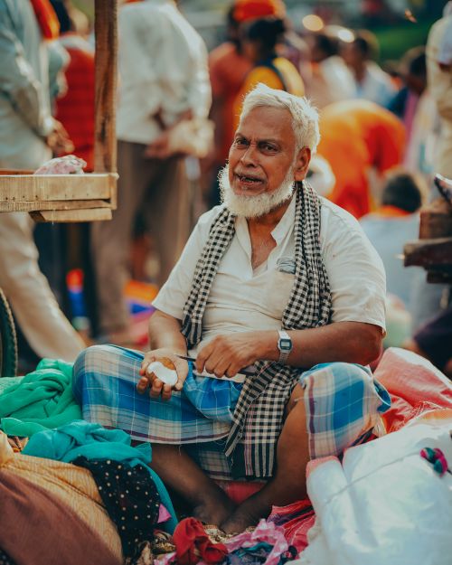 Free Senior man with gray hair sitting in a bustling market in Lucknow, India, surrounded by colorful textiles. Stock Photo