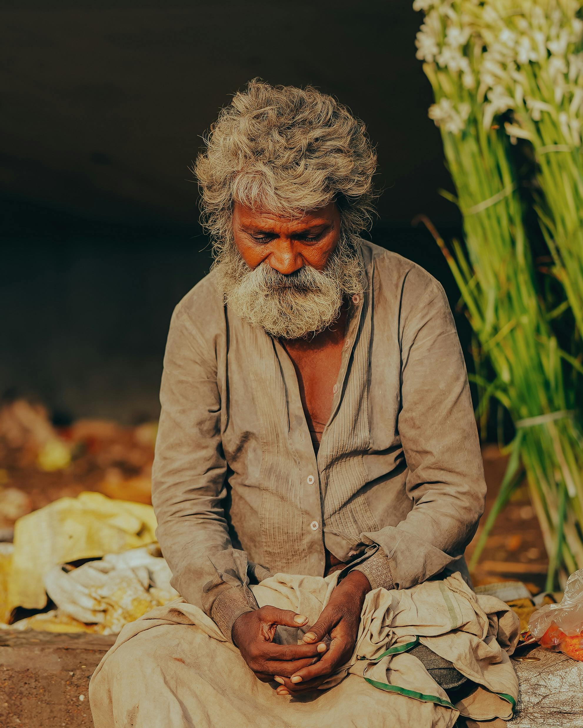 Senior man with gray hair and beard sitting outdoors in Lucknow, India, lost in thought.
