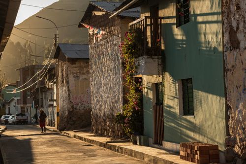 Free Charming Huancavelica street at sunset with a lone figure. Rustic architecture and vivid flowers. Stock Photo