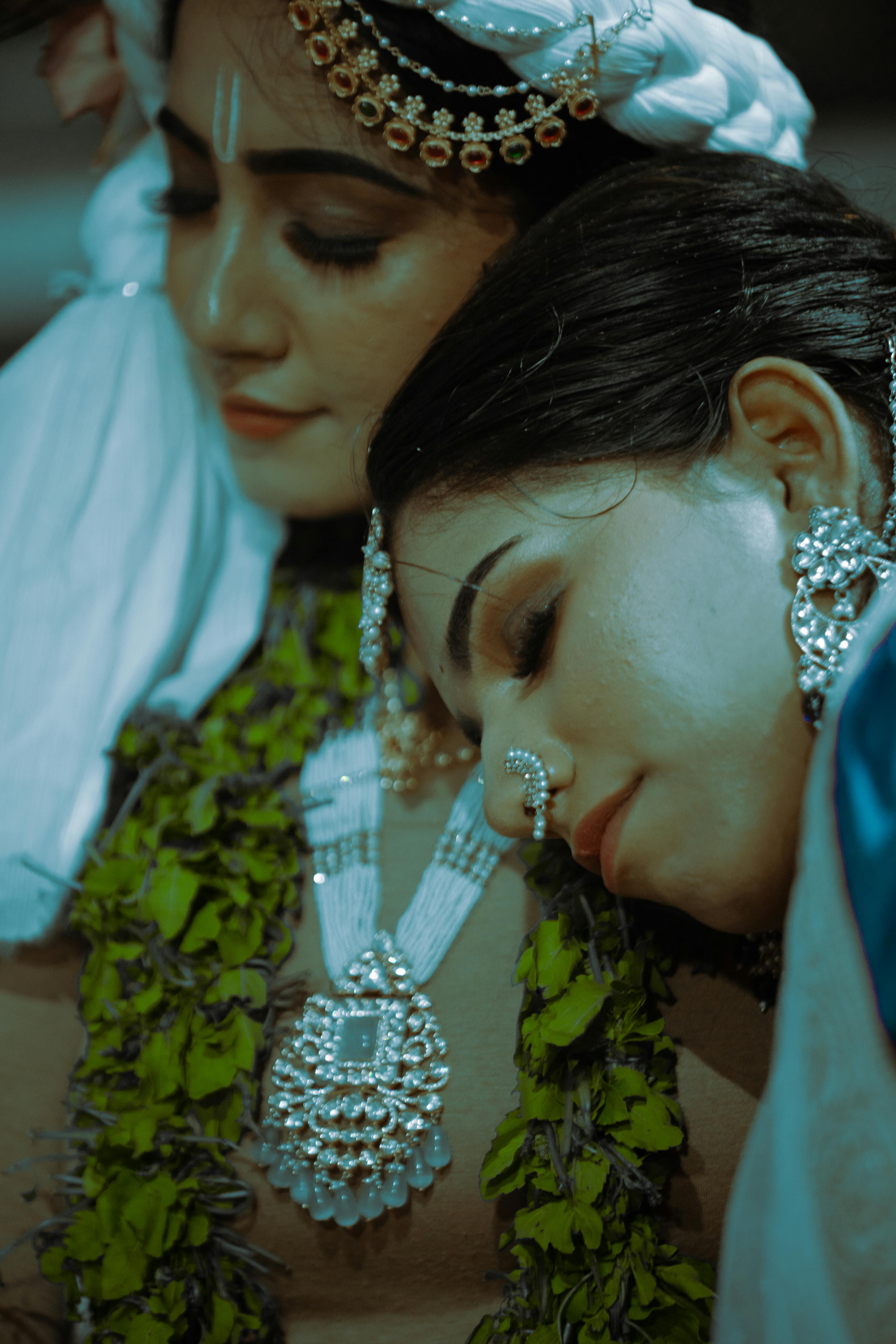 Two women adorned in traditional Indian jewelry and attire in a cultural celebration.