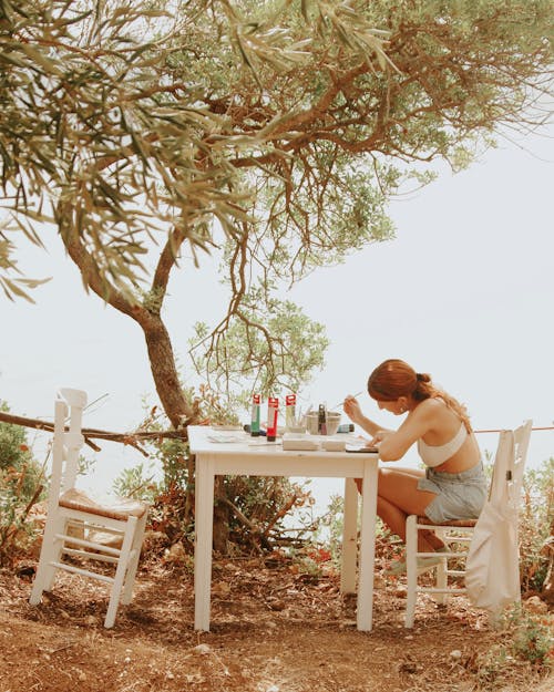 Woman in Bra Sitting by Table under Tree and Painting