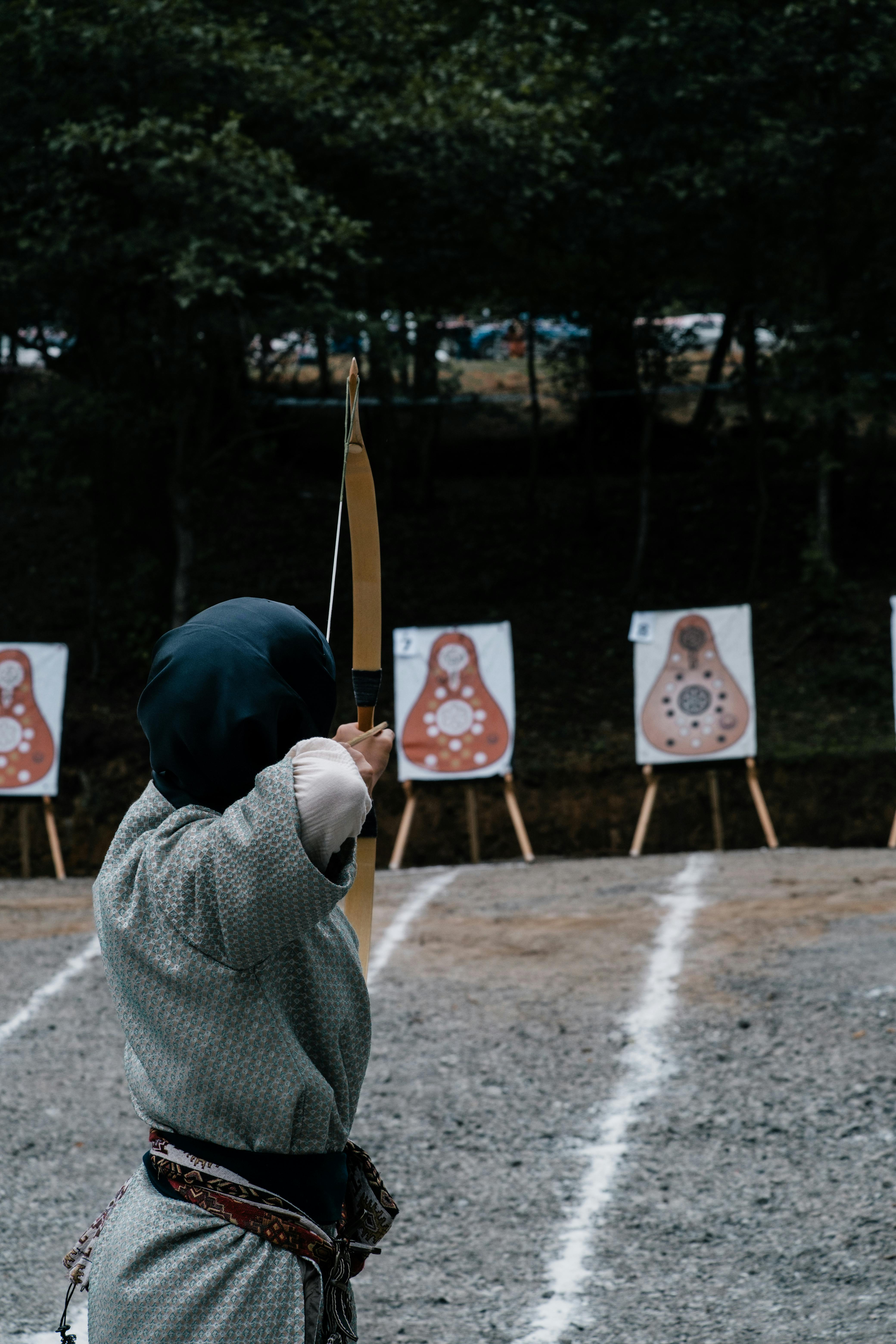 A person practicing traditional archery outdoors aiming at targets in a forest setting.