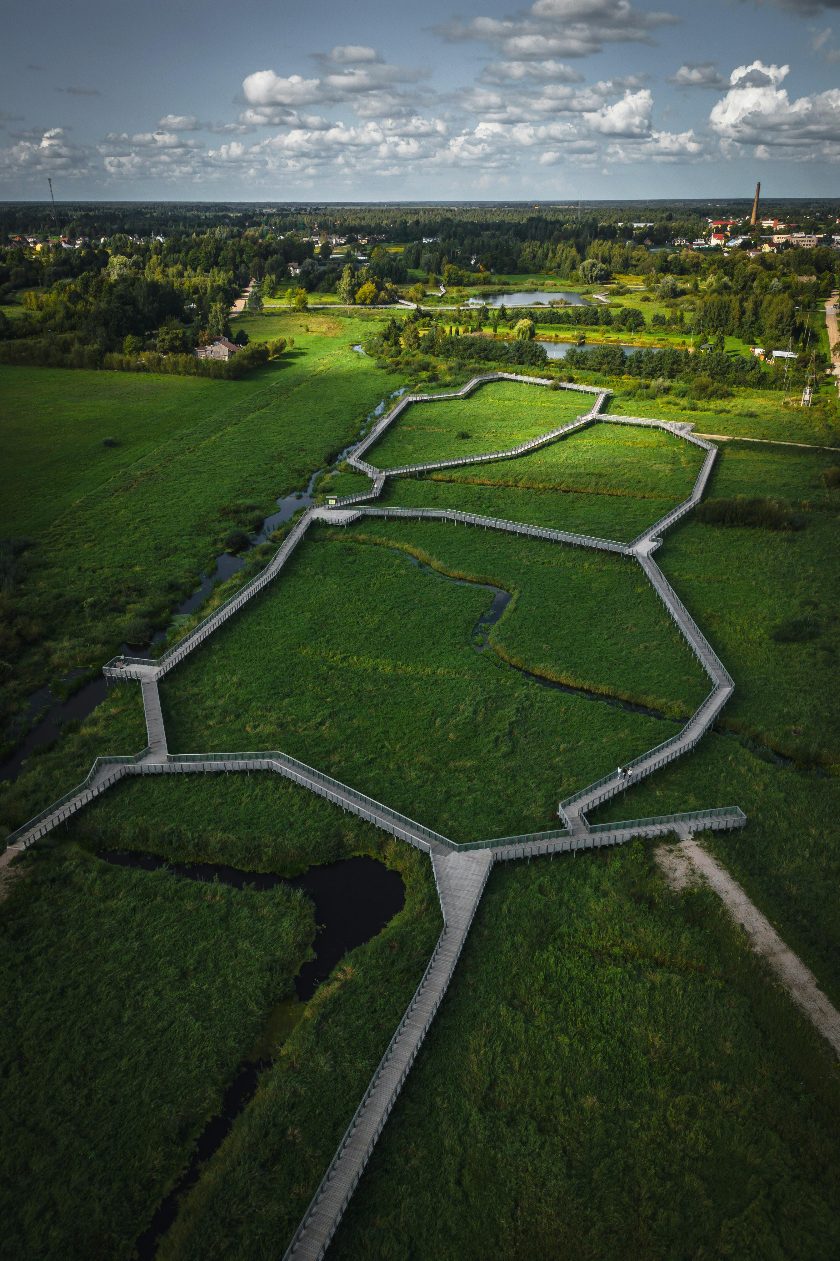 High-angle aerial shot of a lush green countryside with distinct bordered footpaths under a clear sky.