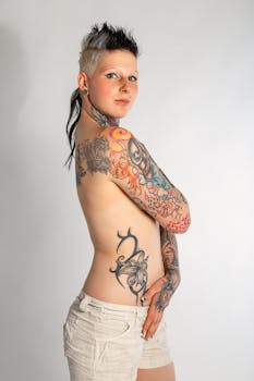Tattooed woman posing topless in studio with elegant fashion style.