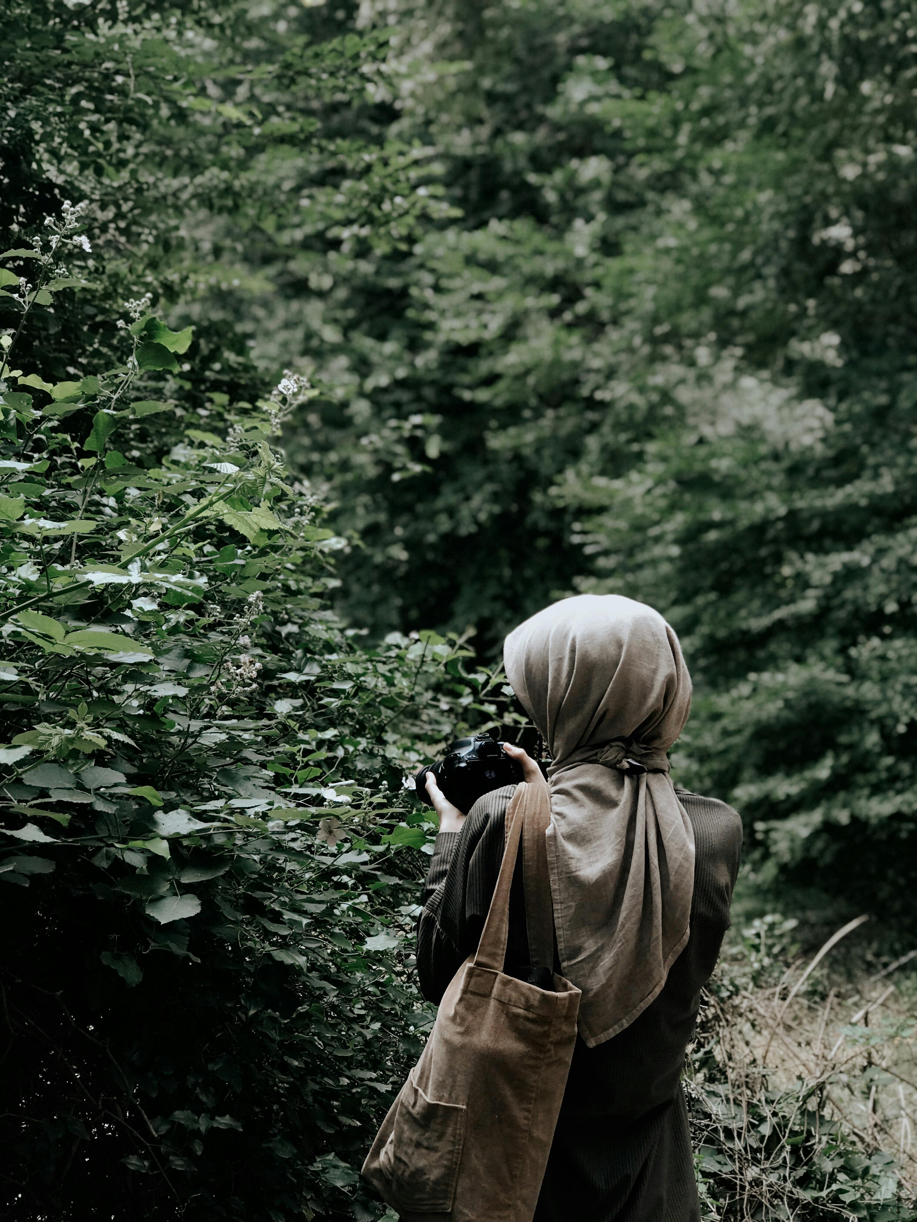 Back view of a woman in a forest taking a photo with lush foliage surrounding her.