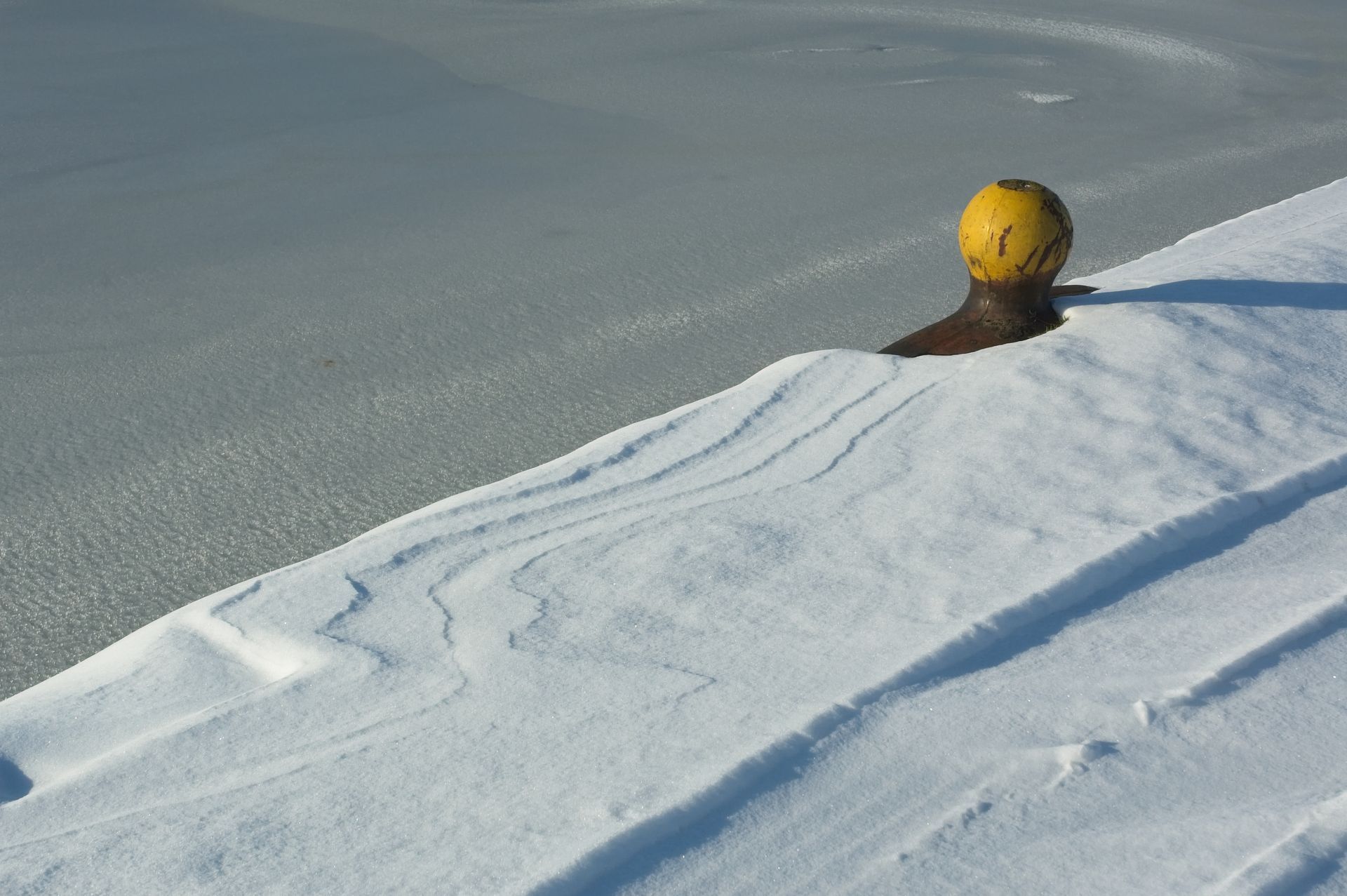 A snow-covered bollard in a frozen harbor. Captures the serene winter scene.