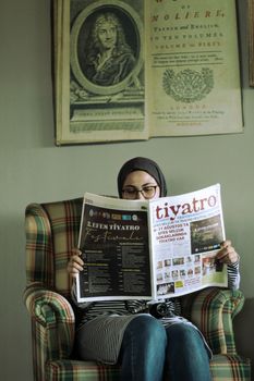 Woman in hijab reading a newspaper in a cozy armchair. Relaxed indoor setting. - Fotografer Sidoarjo