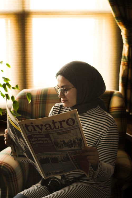 Free Middle Eastern woman in headscarf reading newspaper in cozy room. Stock Photo