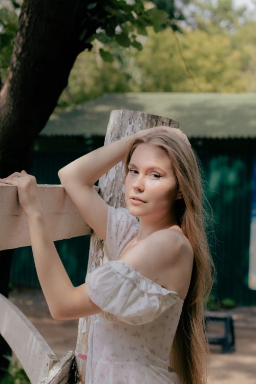 Free A serene portrait of a young woman standing by a fence amidst nature, exuding elegance and grace. Stock Photo