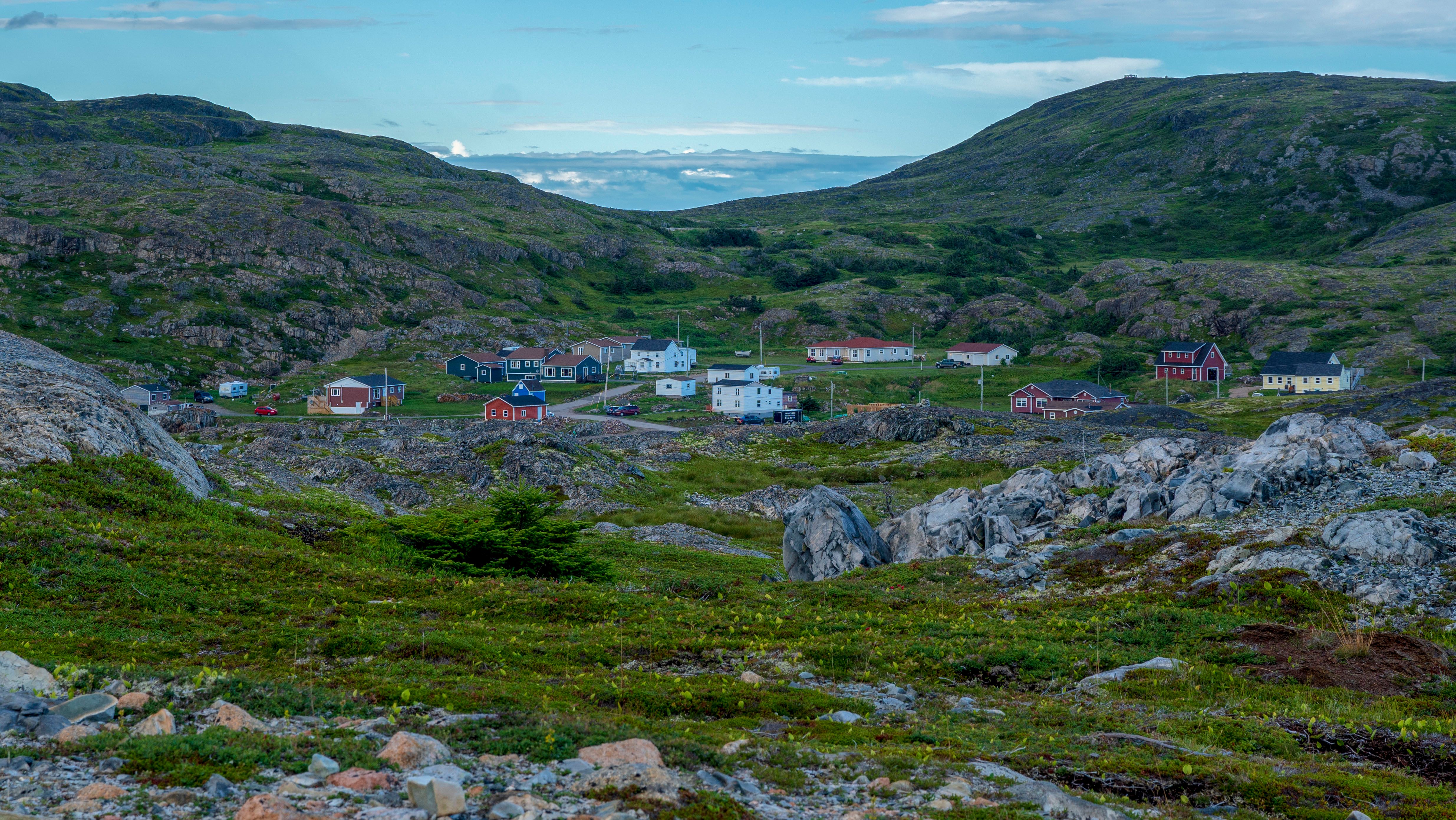 Idyllic village nestled in a rocky landscape, surrounded by lush green hills under a clear sky.