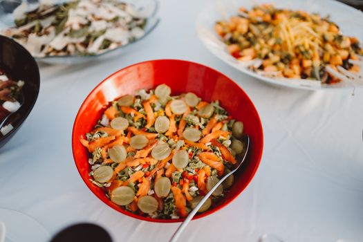 Colorful salad with vegetables and grapes in a red bowl on a white tablecloth, perfect for healthy meals.