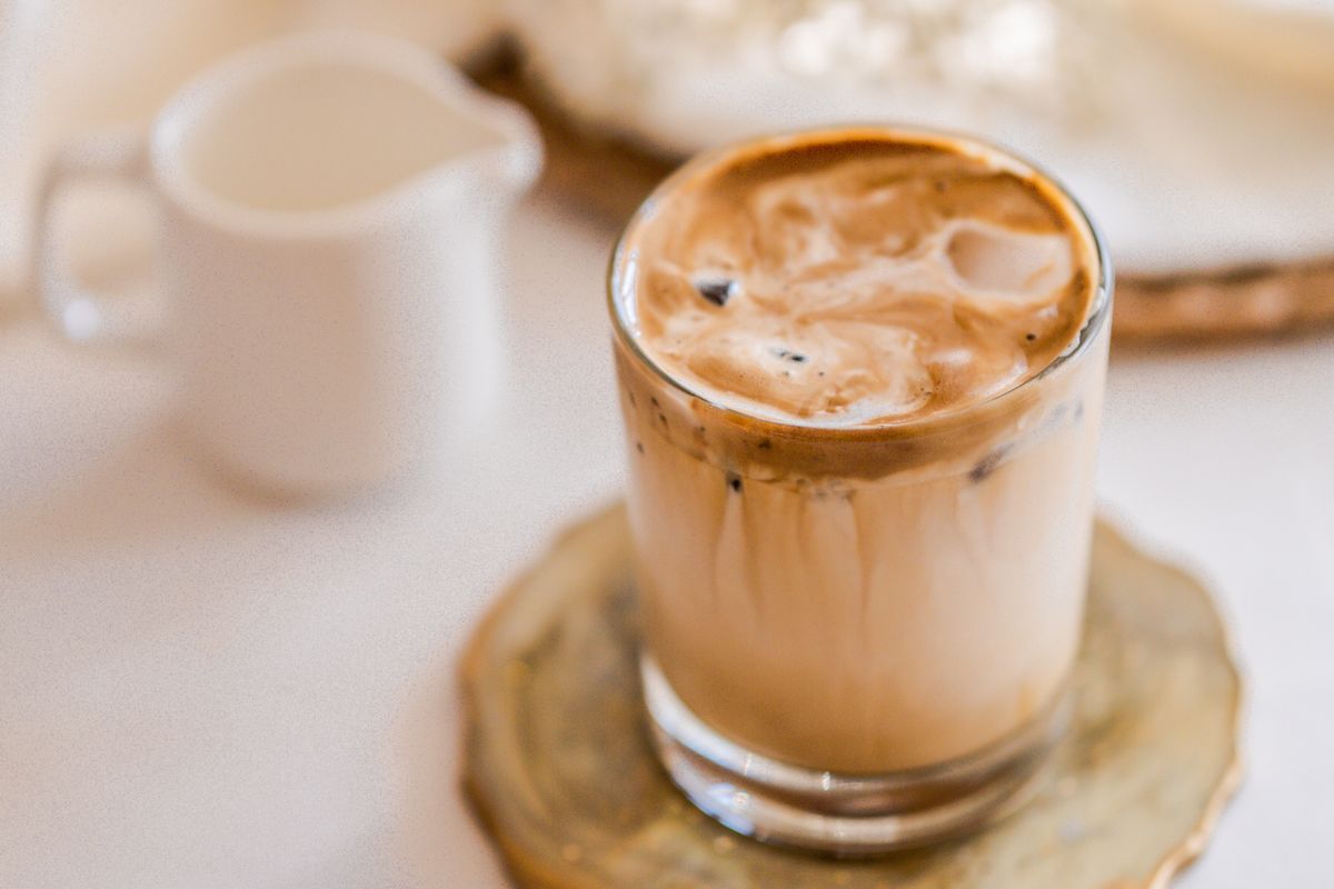 Iced coffee in a clear glass with cream and syrup on a bright cafe table