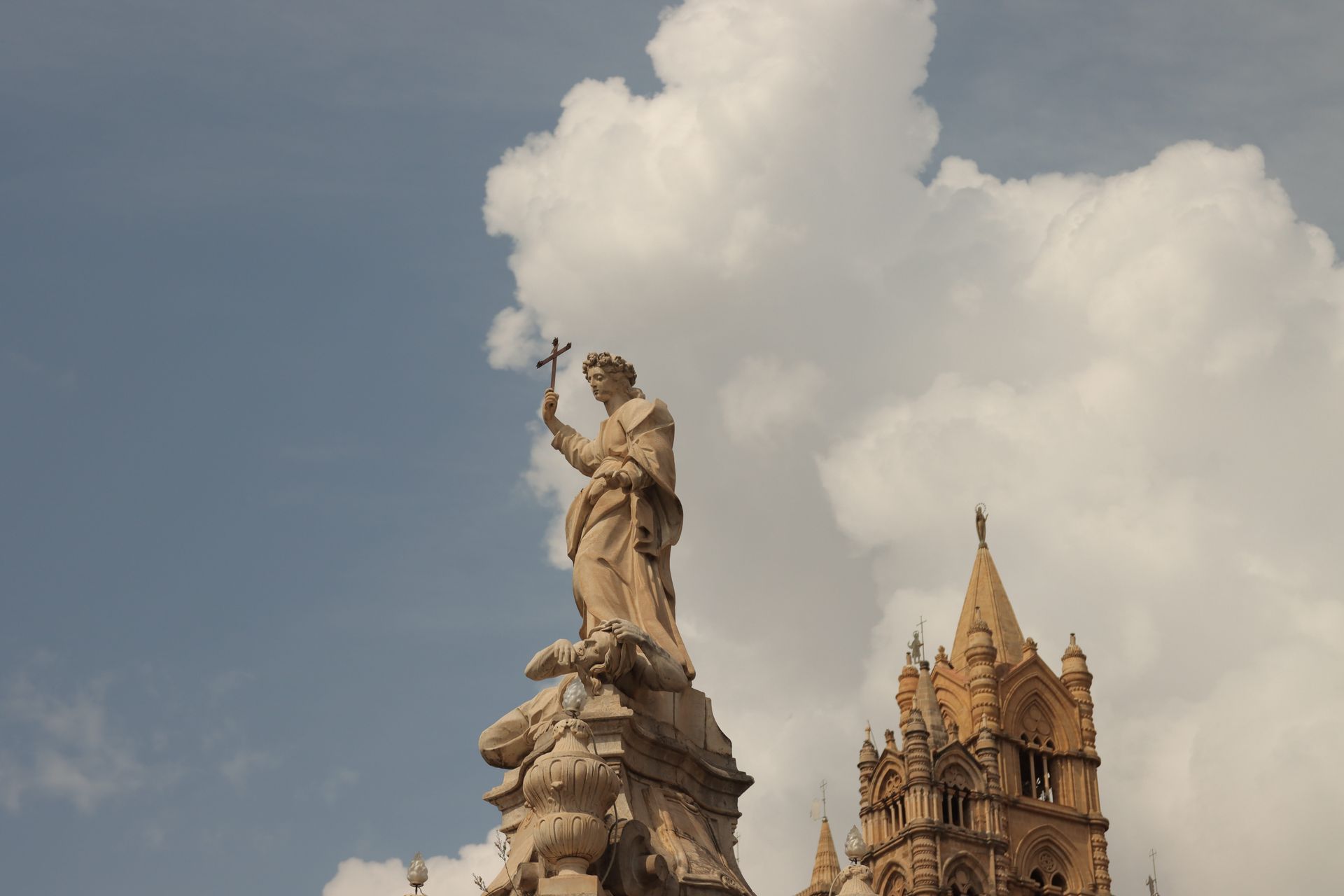 Statue with a cross overlooking Palermo Cathedral against a cloudy sky in Sicily, Italy.