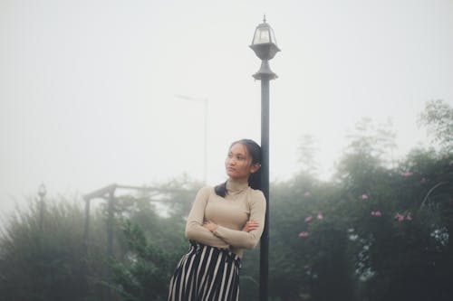 Woman Leaning against a Lamppost, and Trees in Mist in Background