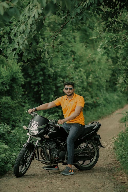 Man Wearing an Orange T-Shirt Posing on a Motorbike against Green Bushes