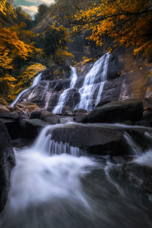 Free Beautiful waterfall cascading through rocks in West Java, Indonesia, surrounded by golden leaves. Stock Photo