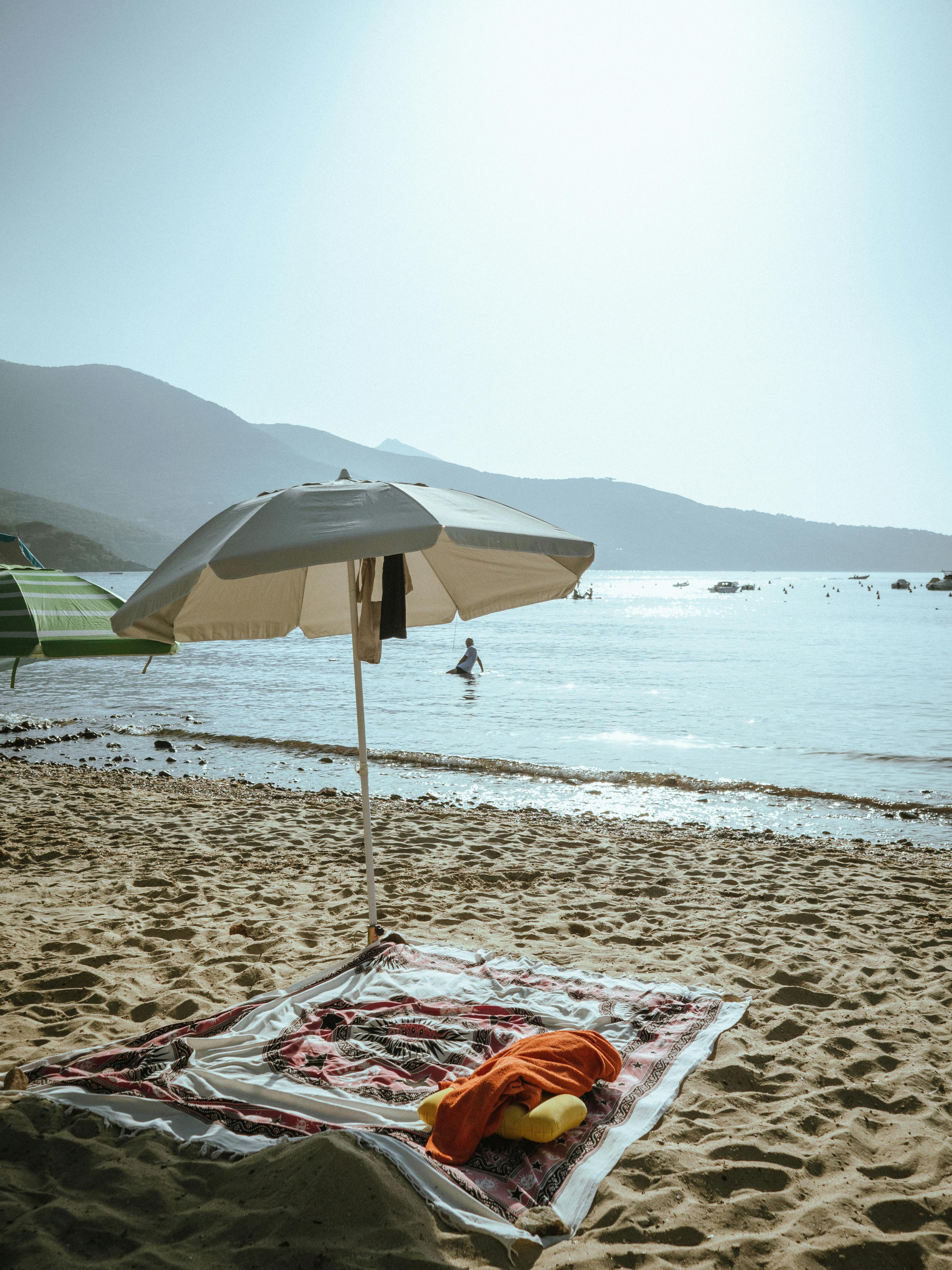 A beach blanket and an umbrella on the sand · Free Stock Photo