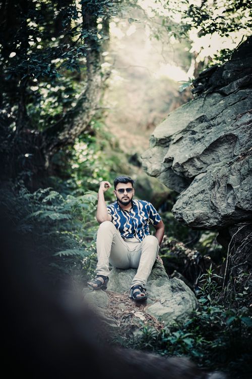 Free Fashionable man in a forest, sitting on rocks, embodies modern outdoor style. Stock Photo