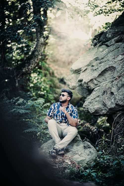 Free Fashionable man in sunglasses sitting on rocks in a forest, surrounded by green foliage. Stock Photo