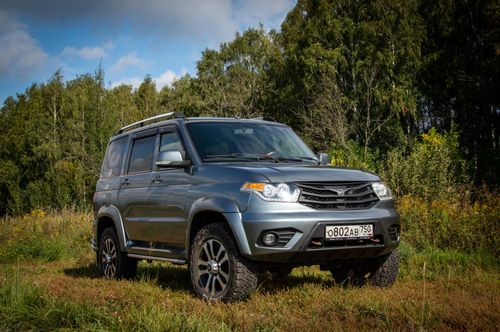 Free Silver SUV parked in a rural meadow surrounded by trees under a clear sky. Stock Photo