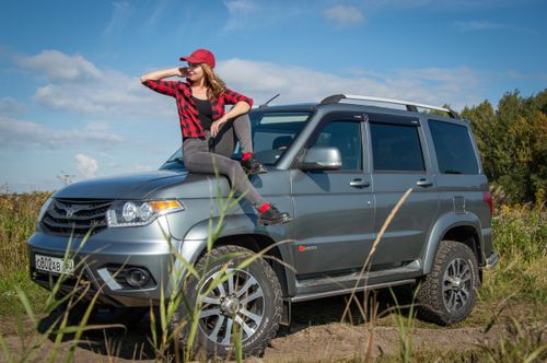 Free Young woman in red cap sitting on a silver SUV with rural backdrop. Stock Photo
