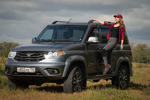 Free A woman confidently poses on a silver SUV in a rural setting on a sunny day. Stock Photo