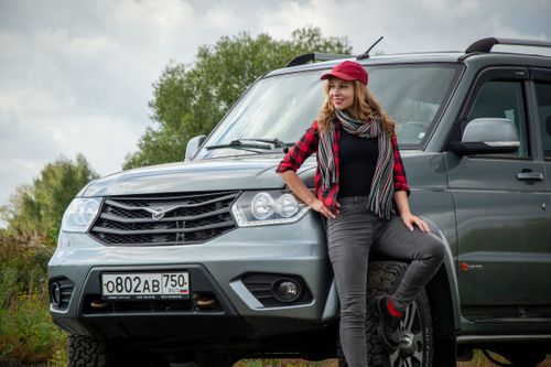 Free Smiling woman in red cap leaning on SUV with outdoor background. Stock Photo