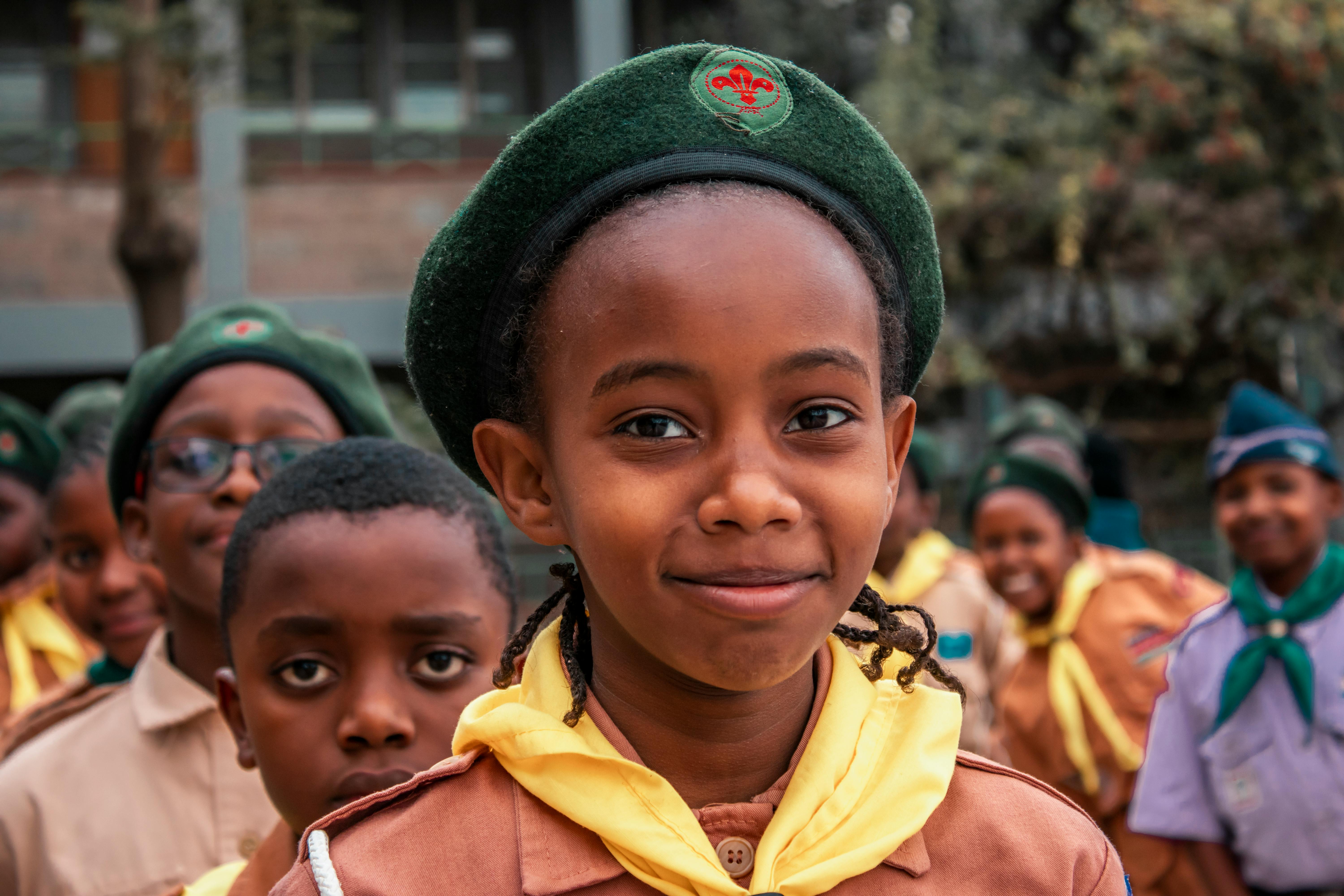 A smiling girl scout in uniform with her friends standing outdoors, ready for adventure.