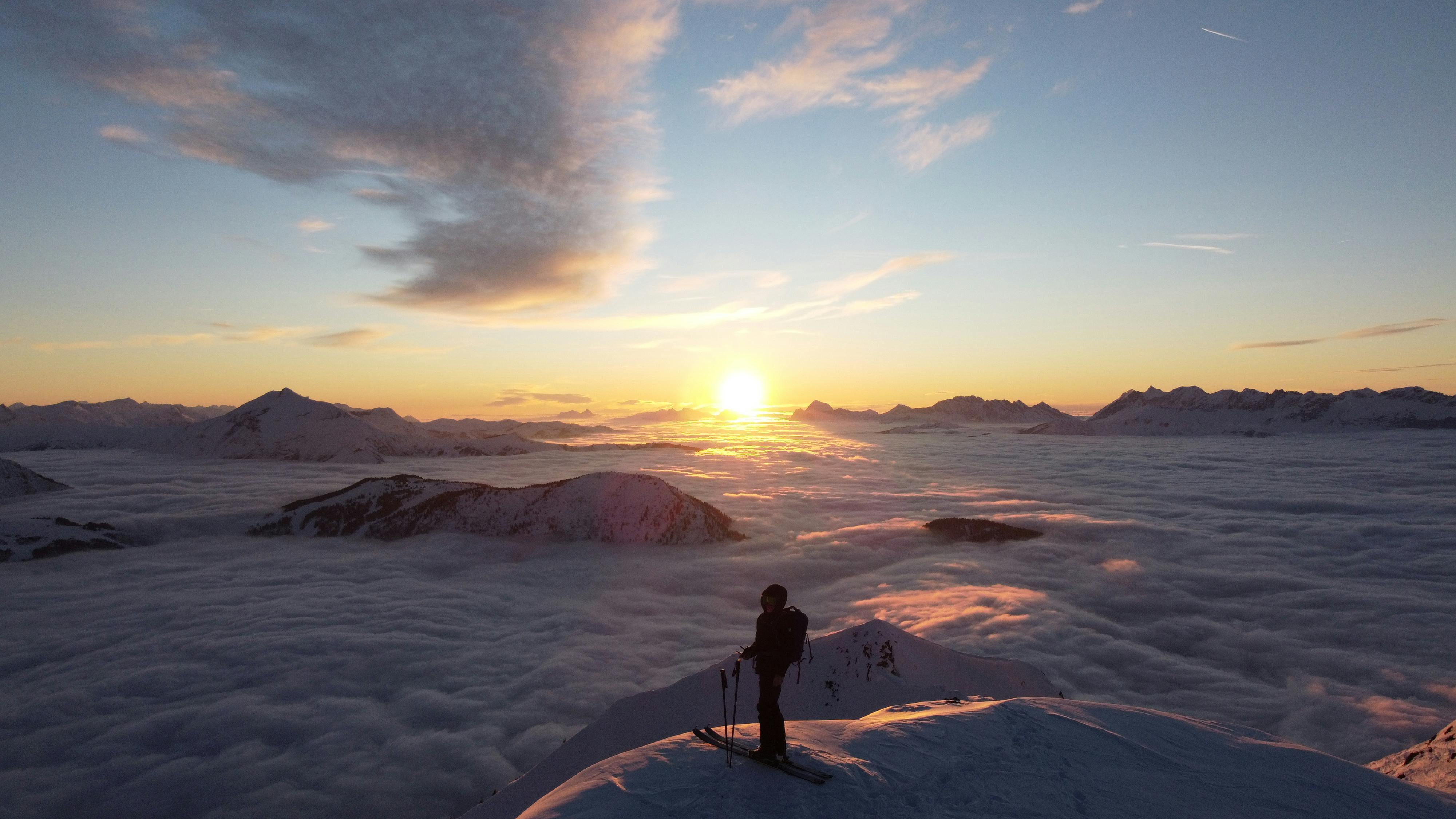 Breathtaking sunrise view over the Alps with a skier silhouetted atop a snowy peak.