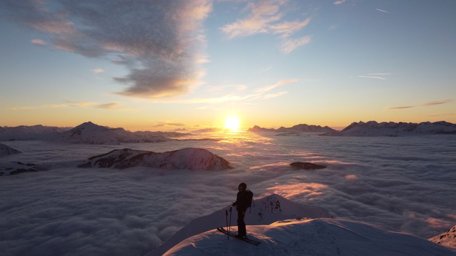 Breathtaking sunrise view over the Alps with a skier silhouetted atop a snowy peak.