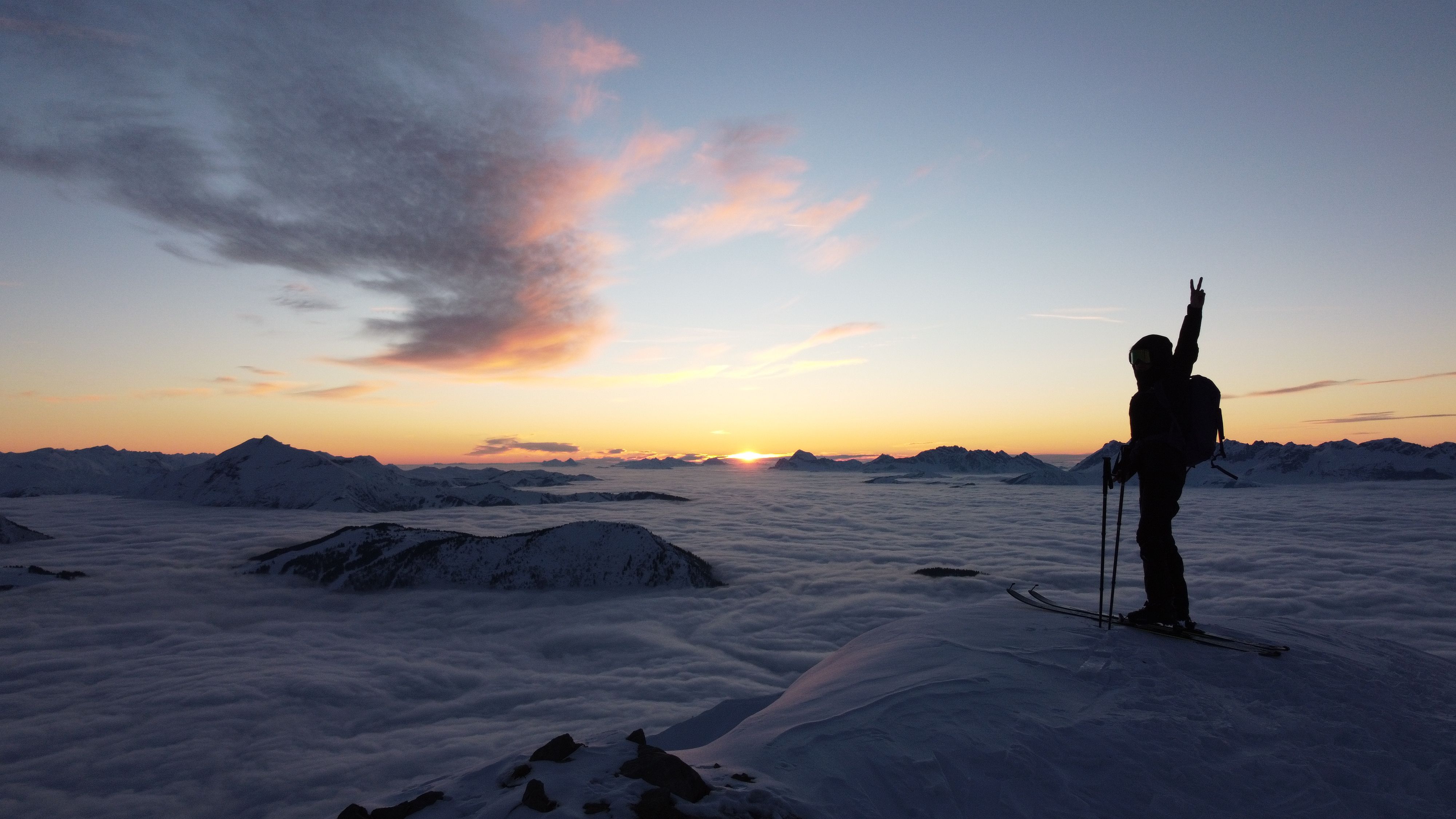 A skier celebrates at sunrise atop a snow-covered summit in the French Alps, capturing an adventurous moment.