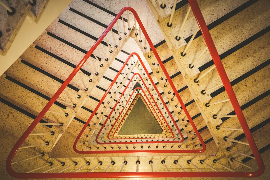 Triangular staircase with red handrails showing modern geometric architecture indoors.