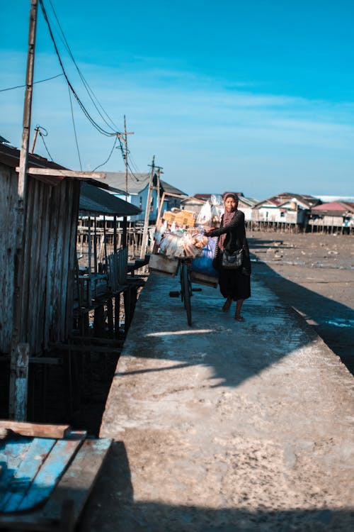 Woman Walking with a Bicycle Overloaded with Goods in a Seashore Village