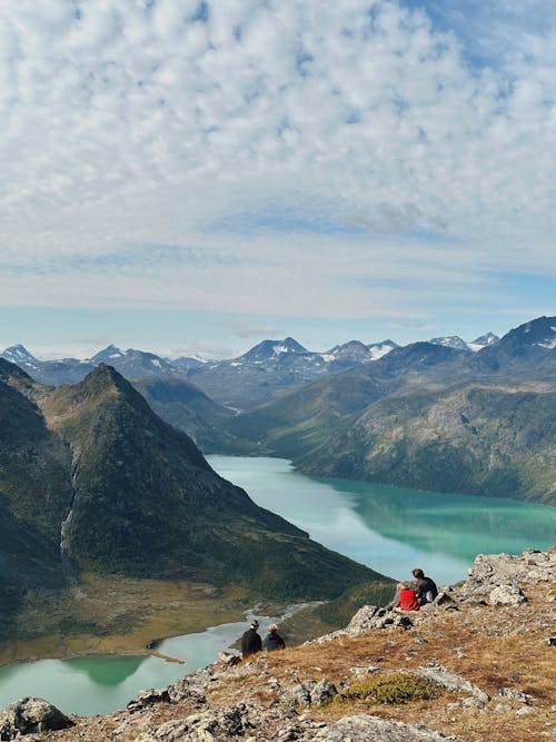 People Sitting on Rocks over River in Mountains