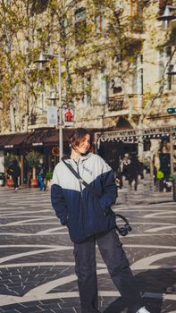 Smiling woman in a jacket standing on a stylish street in Baku, Azerbaijan, enjoying urban vibes.