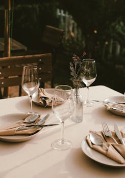 Chic outdoor dining setup in Đà Lạt with cutlery, plates, and wine glasses under warm lighting.