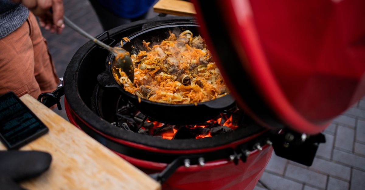 A delicious pilaf is being prepared on a kamado grill outdoors, showcasing vibrant culinary skills.