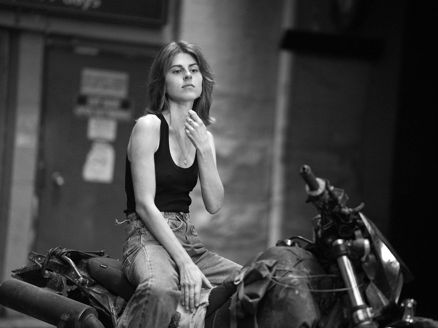 Monochrome photo of a woman posing on a motorcycle against an urban background.