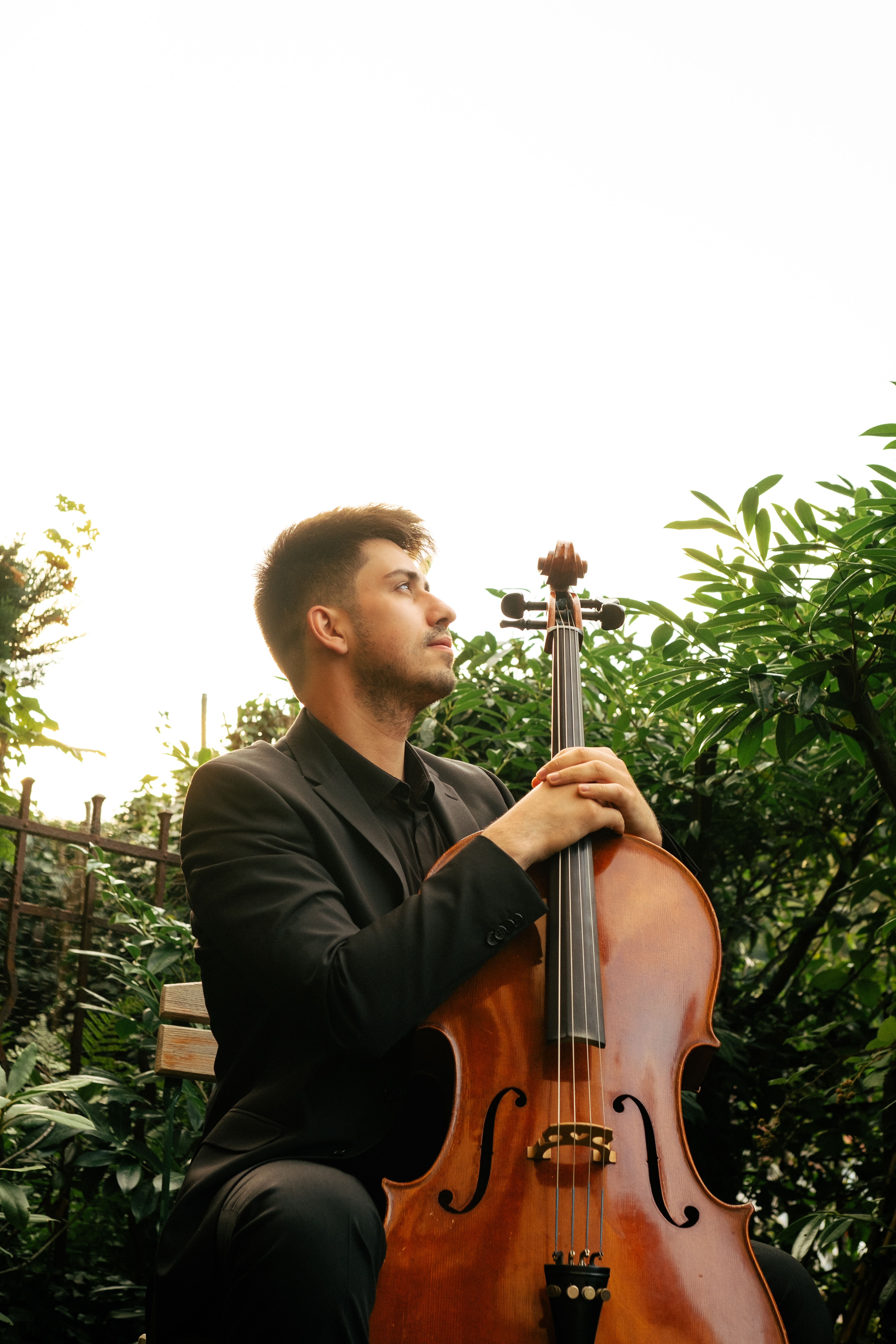 A cellist in a suit poses outdoors with his cello, exuding elegance and musical passion.