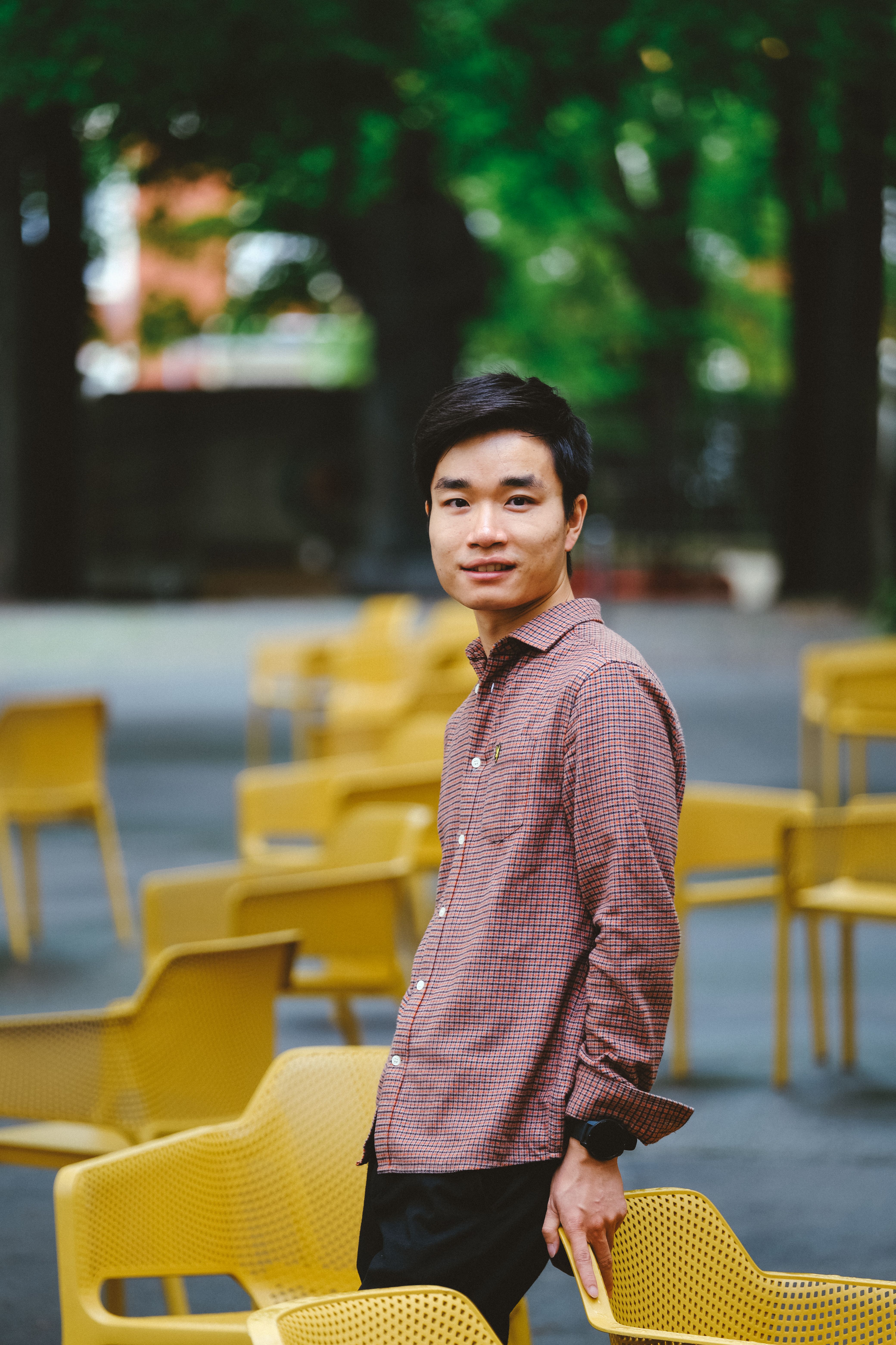 A young adult poses among yellow chairs in a vibrant outdoor park, exuding a lively and fresh vibe.