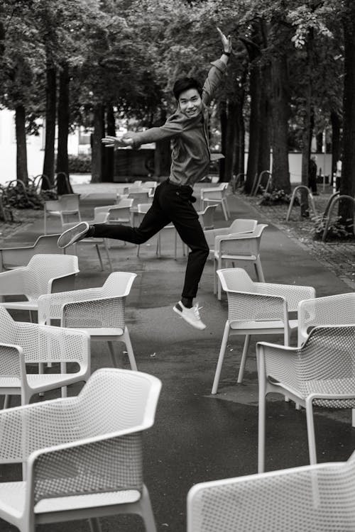 Man in Shirt Jumping among Chairs