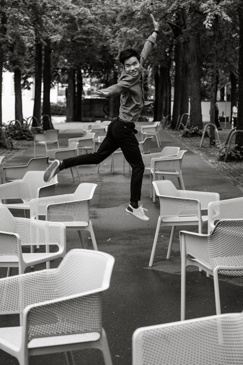 Smiling Man in Shirt Jumping among Chairs