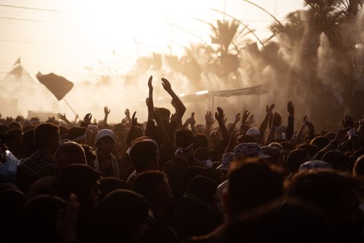 Silhouetted crowd raising hands during a sunset gathering in Karbala, Iraq.