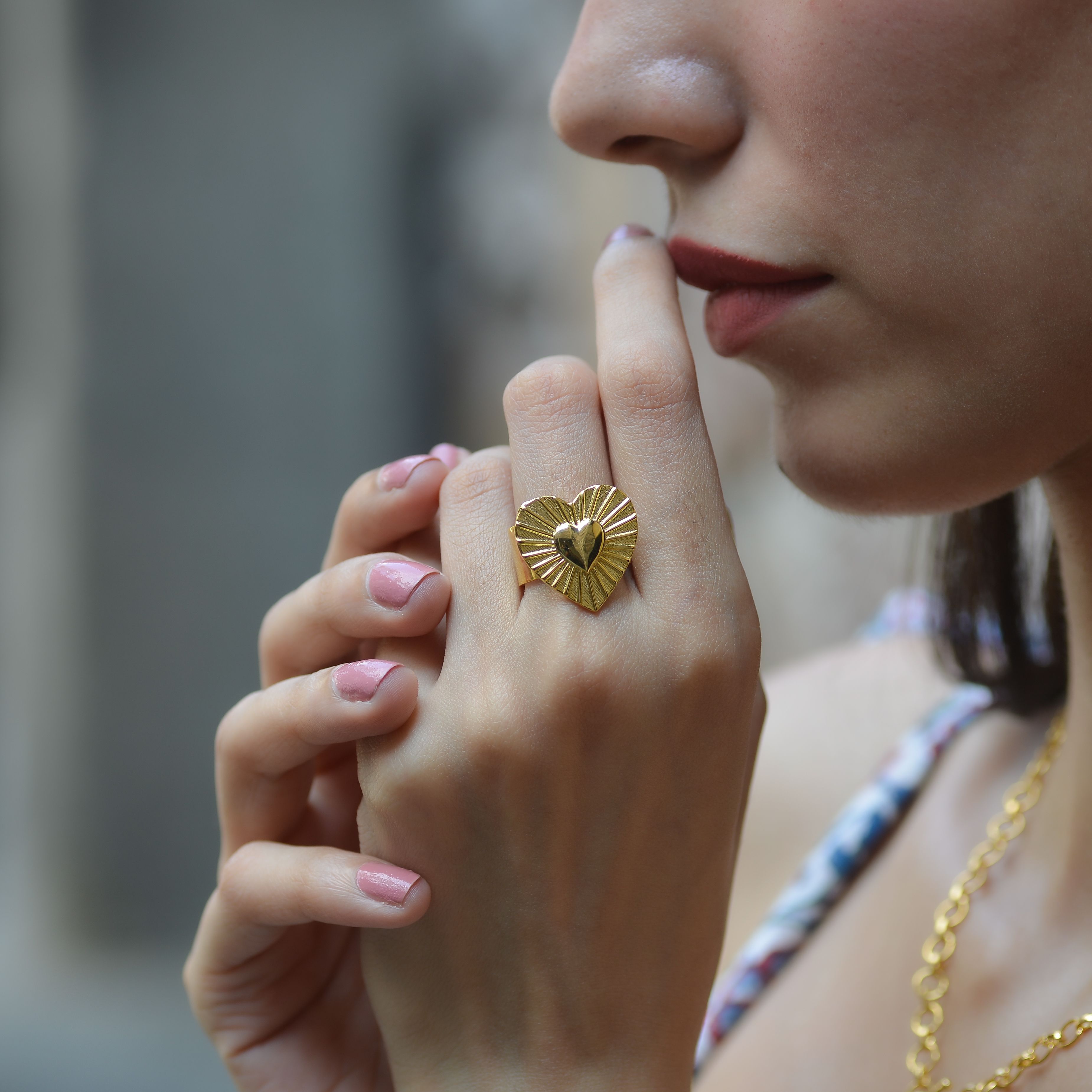 Close-up image of a woman showcasing a gold heart-shaped ring and elegant jewelry.
