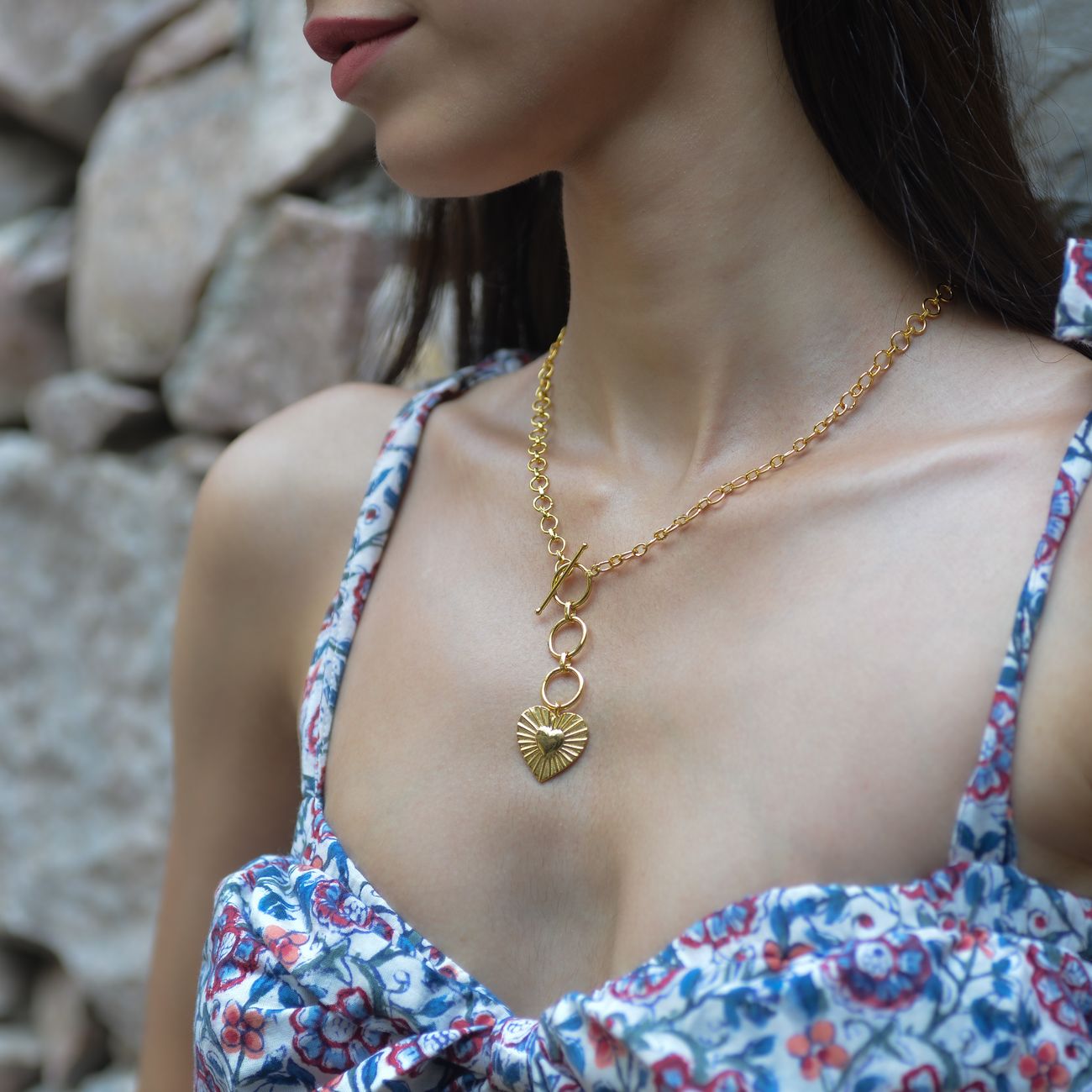 Close-up of a woman wearing a gold heart pendant necklace outdoors.