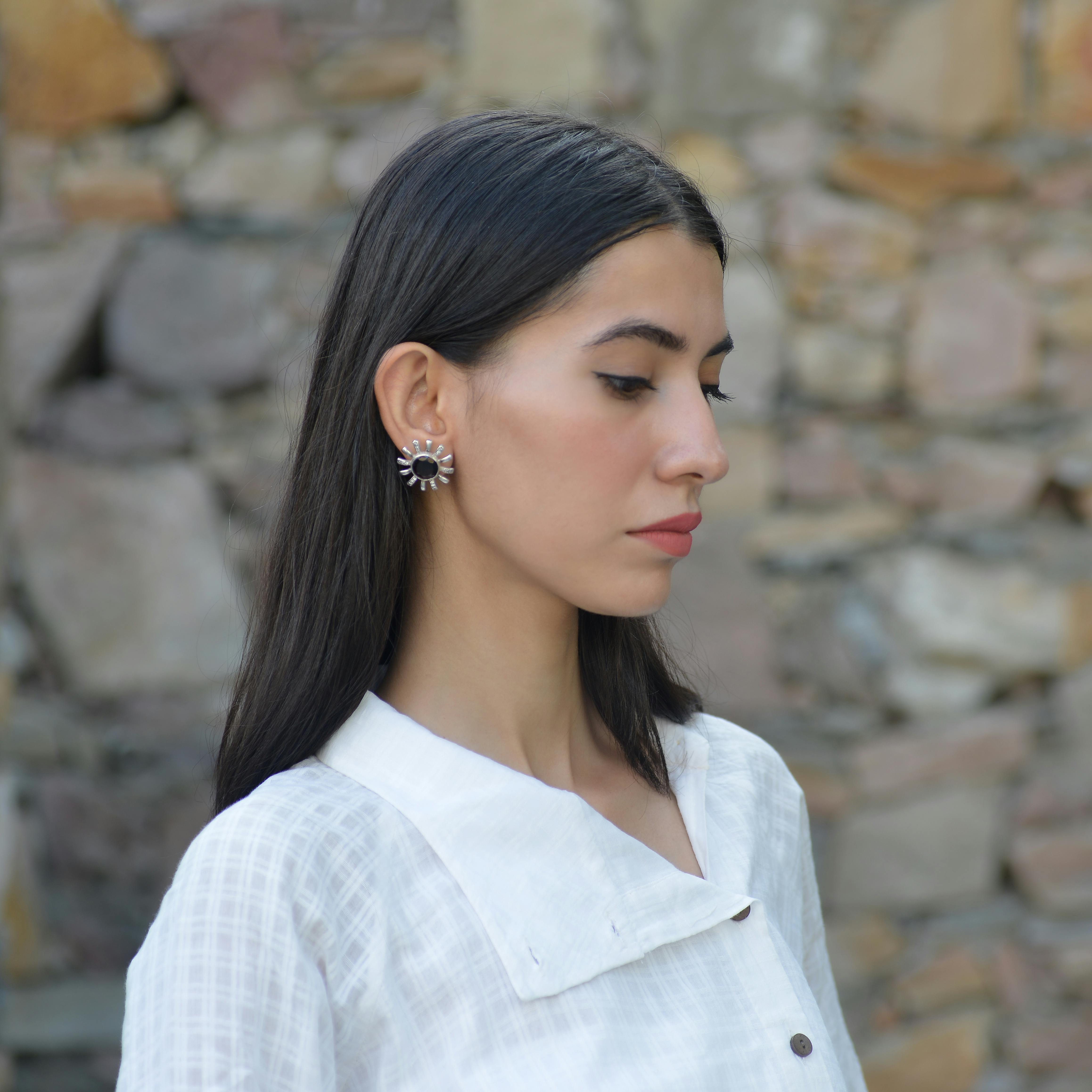Profile of a young woman posing gracefully against a stone wall, wearing elegant earrings.