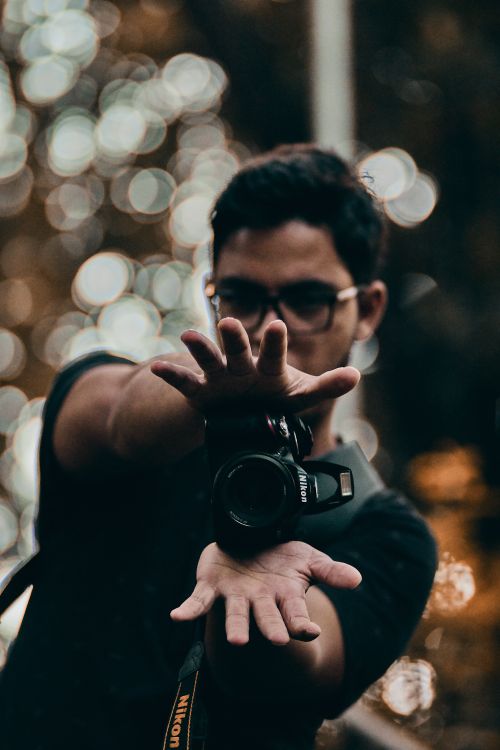 Free Portrait of a young male photographer posing creatively with a camera, surrounded by artistic bokeh lighting. Stock Photo